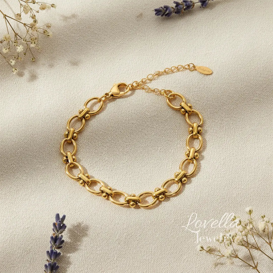 Gold chain bracelet on a soft beige background with lavender and small white flowers.