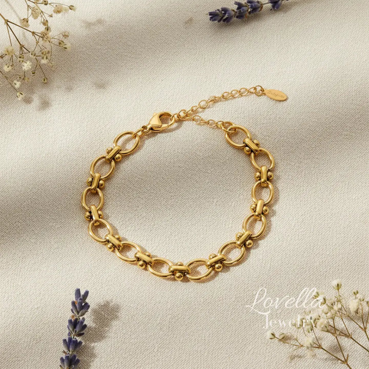 Gold chain bracelet on a soft beige background with lavender and small white flowers.