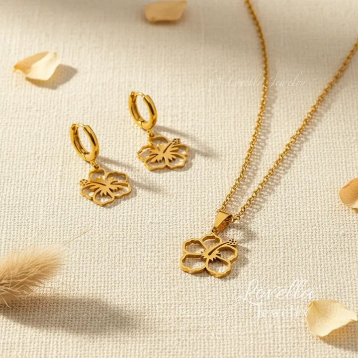 Gold butterfly necklace and earrings on a textured beige surface with dried flowers.