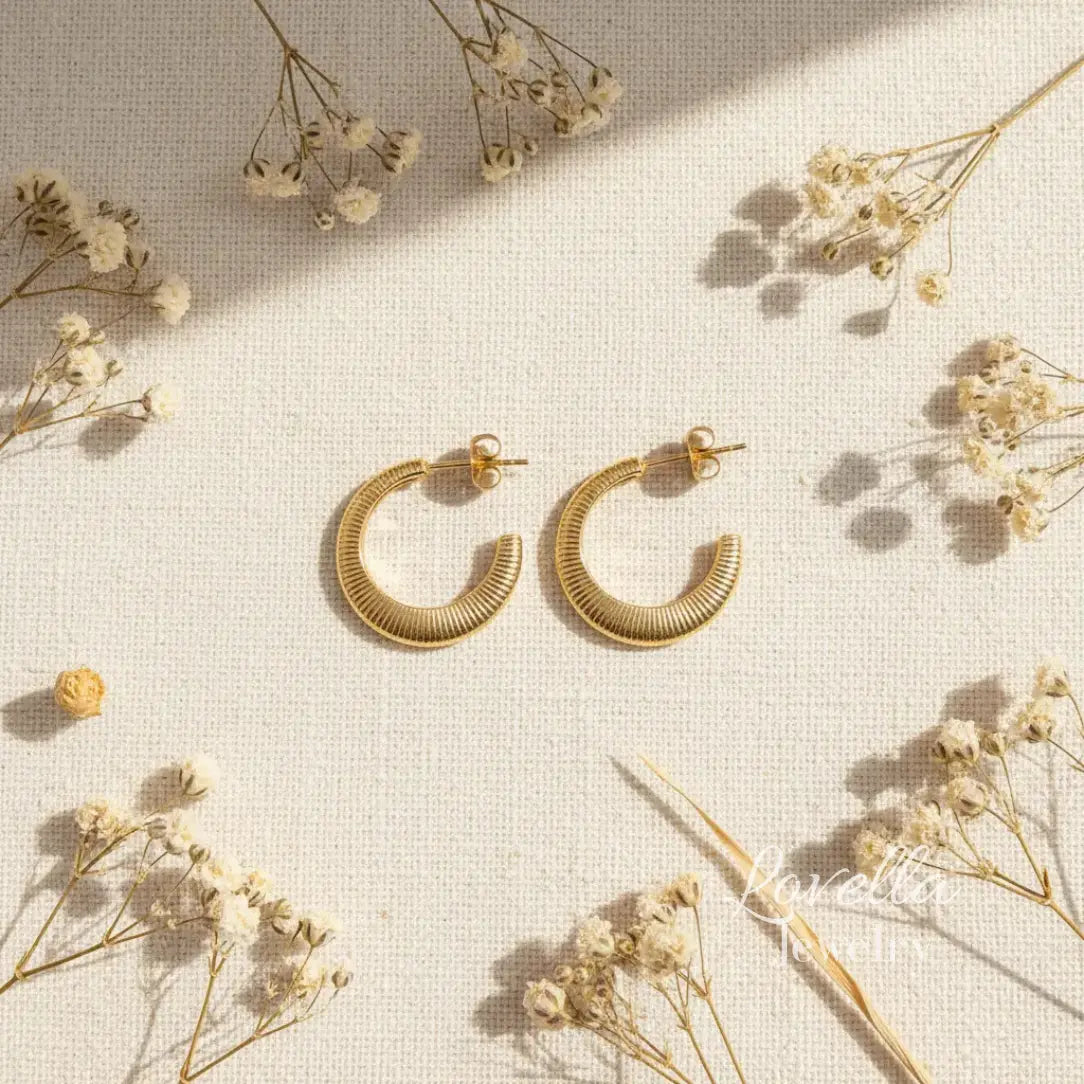 Gold hoop earrings on a light background with dried flowers