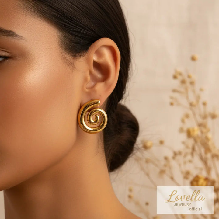 Close-up of a gold spiral earring on an ear with a blurred background and Lovella Jewelry logo.