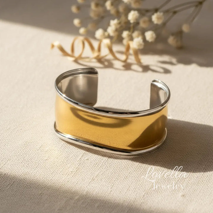 Gold and silver cuff bracelet on a beige fabric background with dried flowers.