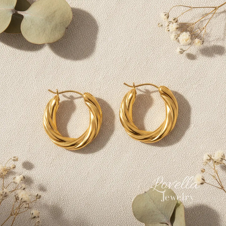 Gold hoop earrings on a light background with eucalyptus leaves and flowers.