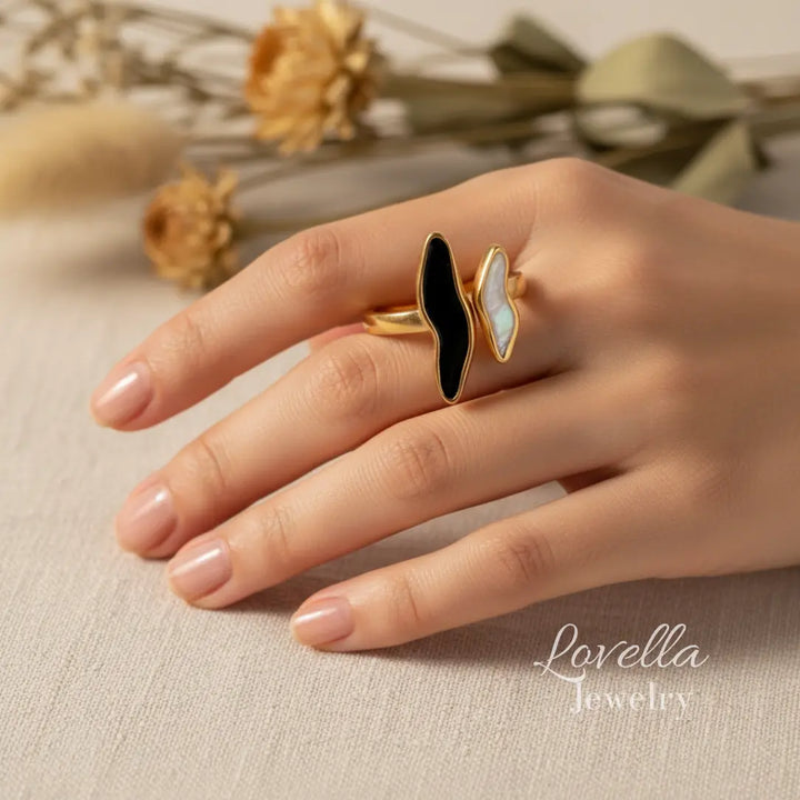 Gold ring with black and white stones on a hand, with 'Lovella Jewelry' branding.