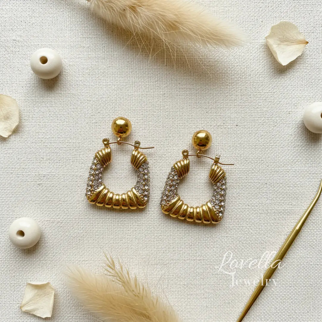 Gold hoop earrings with diamond accents on a light background with decorative elements.