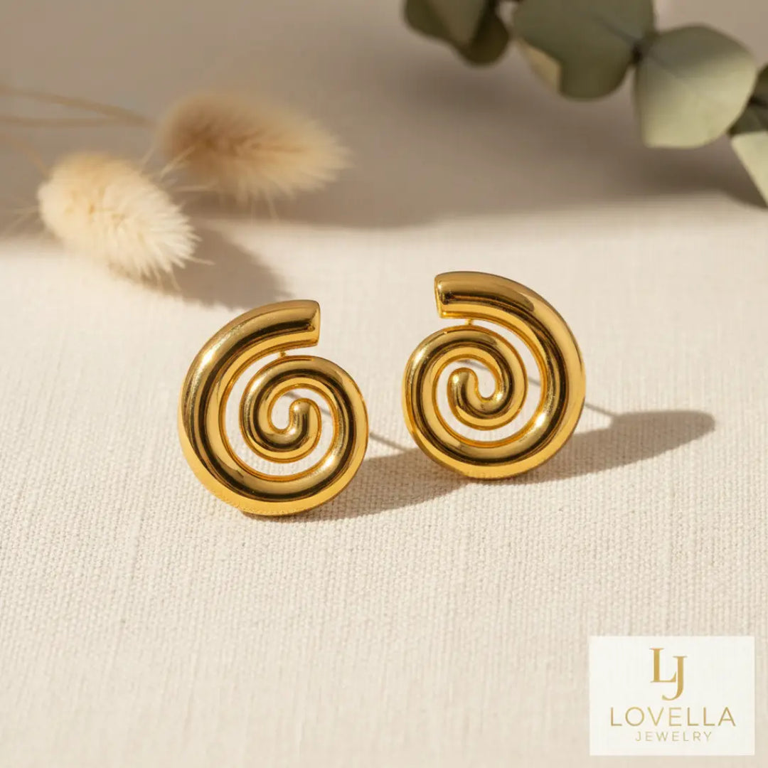 Gold spiral earrings on a beige surface with Lovella Jewelry logo.
