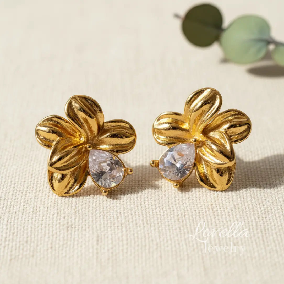 Gold floral earrings with clear gemstones on a beige fabric background