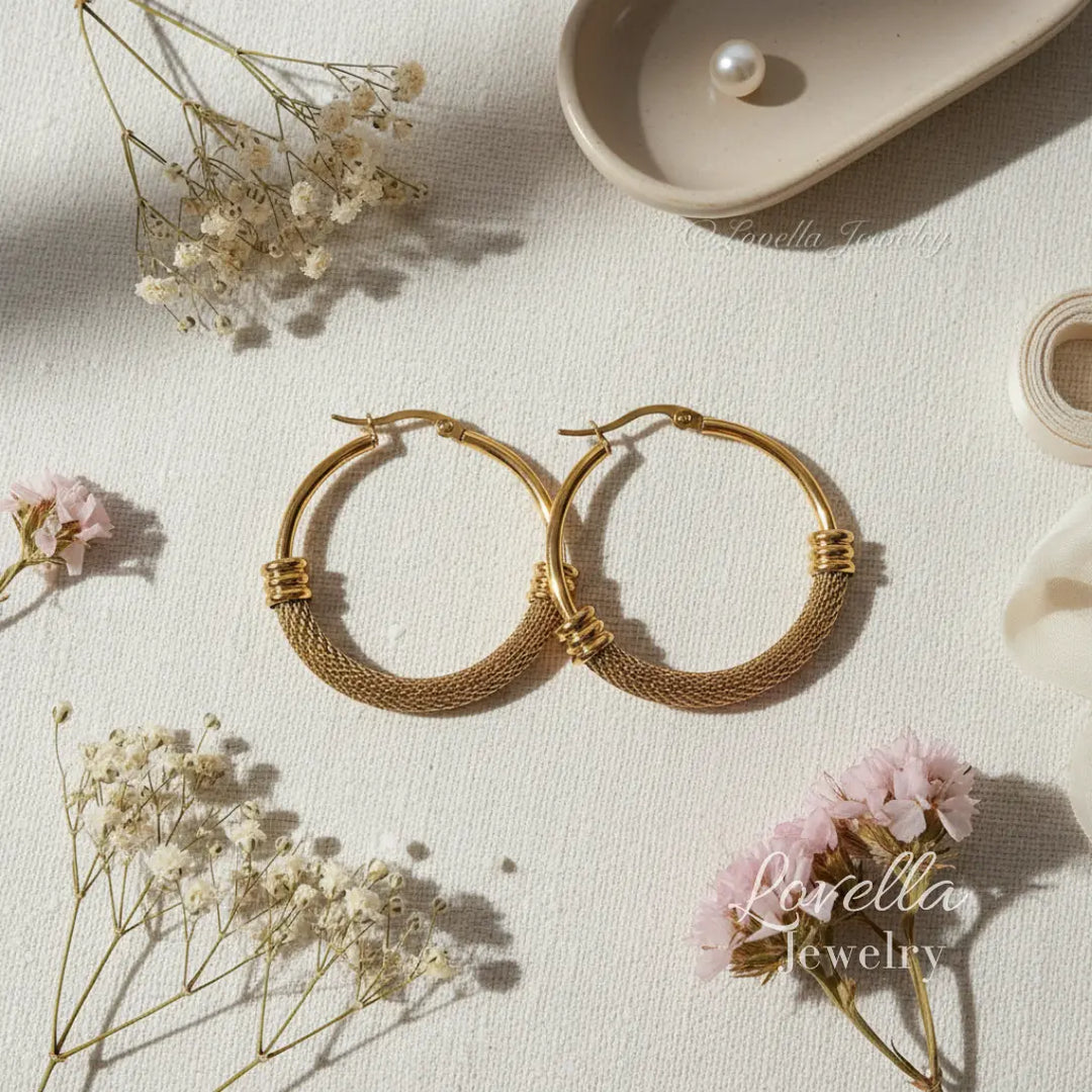 Gold hoop earrings on a light surface with flowers and a pearl.