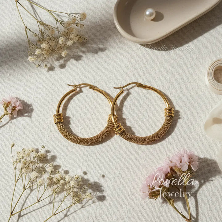 Gold hoop earrings on a light surface with flowers and a pearl.