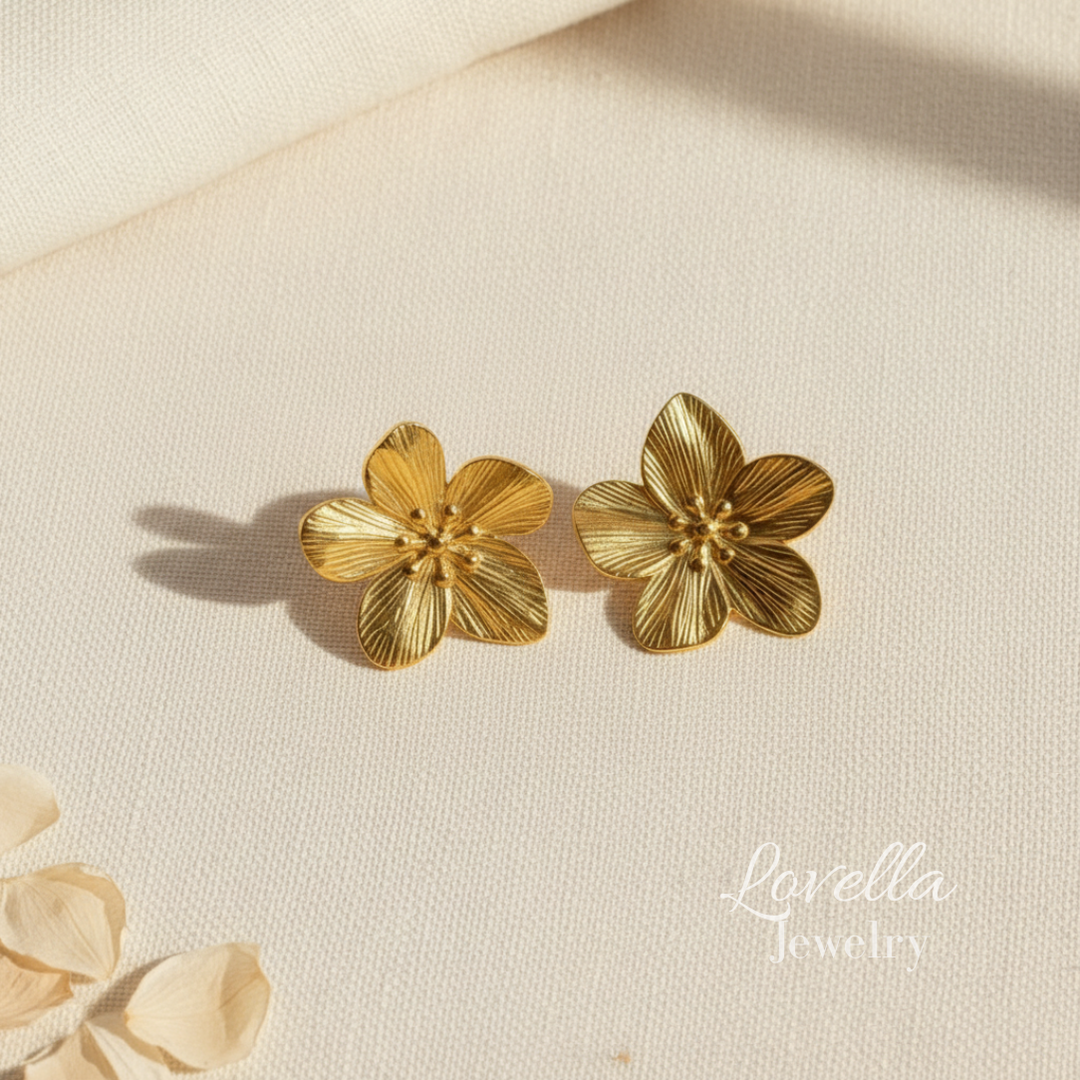 Gold flower-shaped earrings on a beige fabric background with 'Lavelia Jewelry' branding.