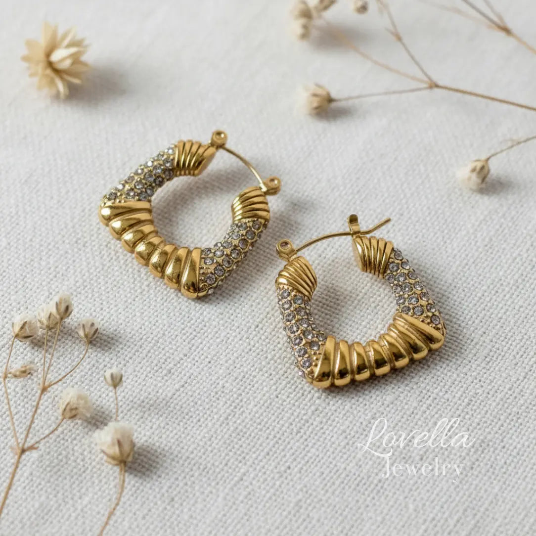 Gold hoop earrings with intricate designs on a light fabric background with dried flowers.