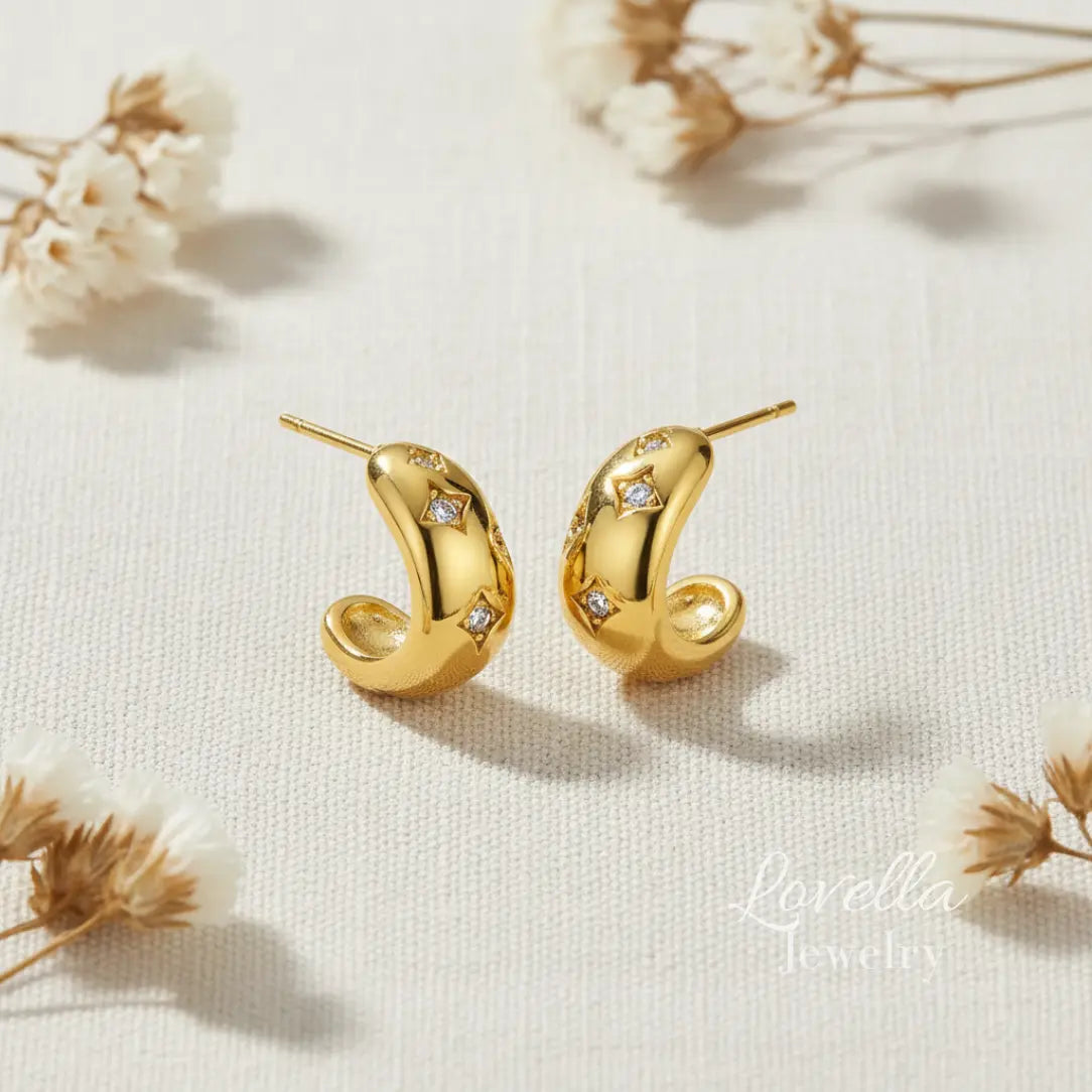 Gold earrings with diamond accents on a light background with dried flowers.