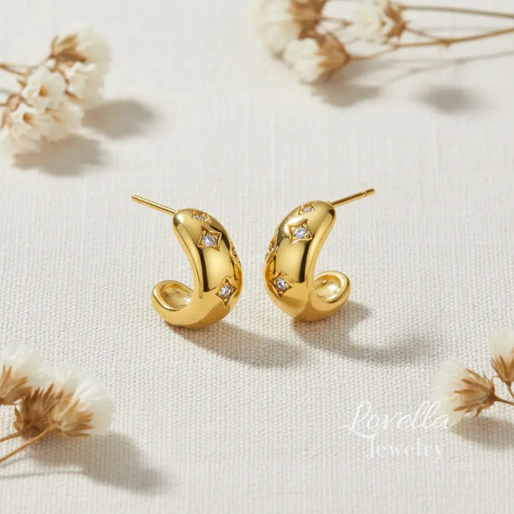 Gold earrings with diamond accents on a light background with dried flowers.