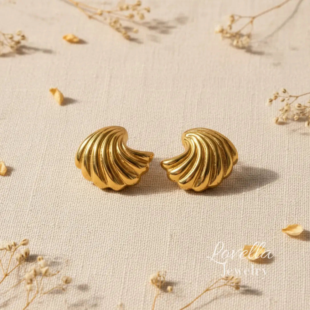 Pair of gold shell-shaped earrings on a textured beige surface with dried flowers.