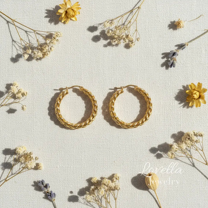 Gold hoop earrings on a light background with dried flowers