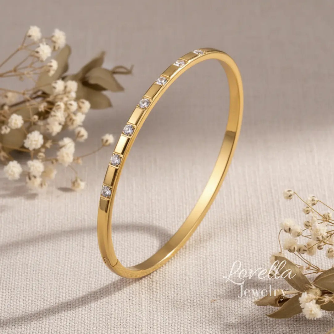 Gold bracelet with small diamonds on a beige background with flowers, featuring Lovella Jewelry.