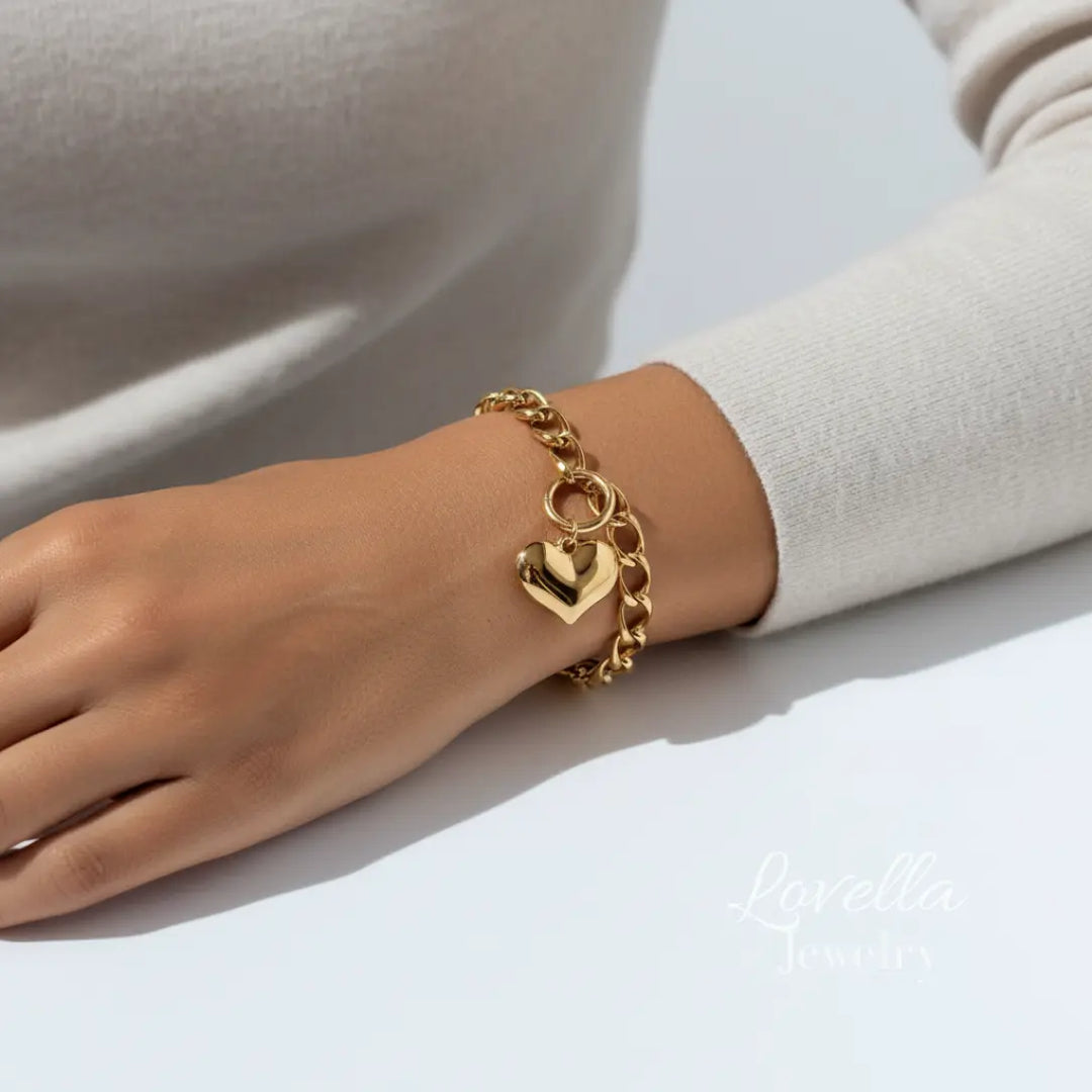 Gold chain bracelet with a heart charm on a wrist against a neutral background