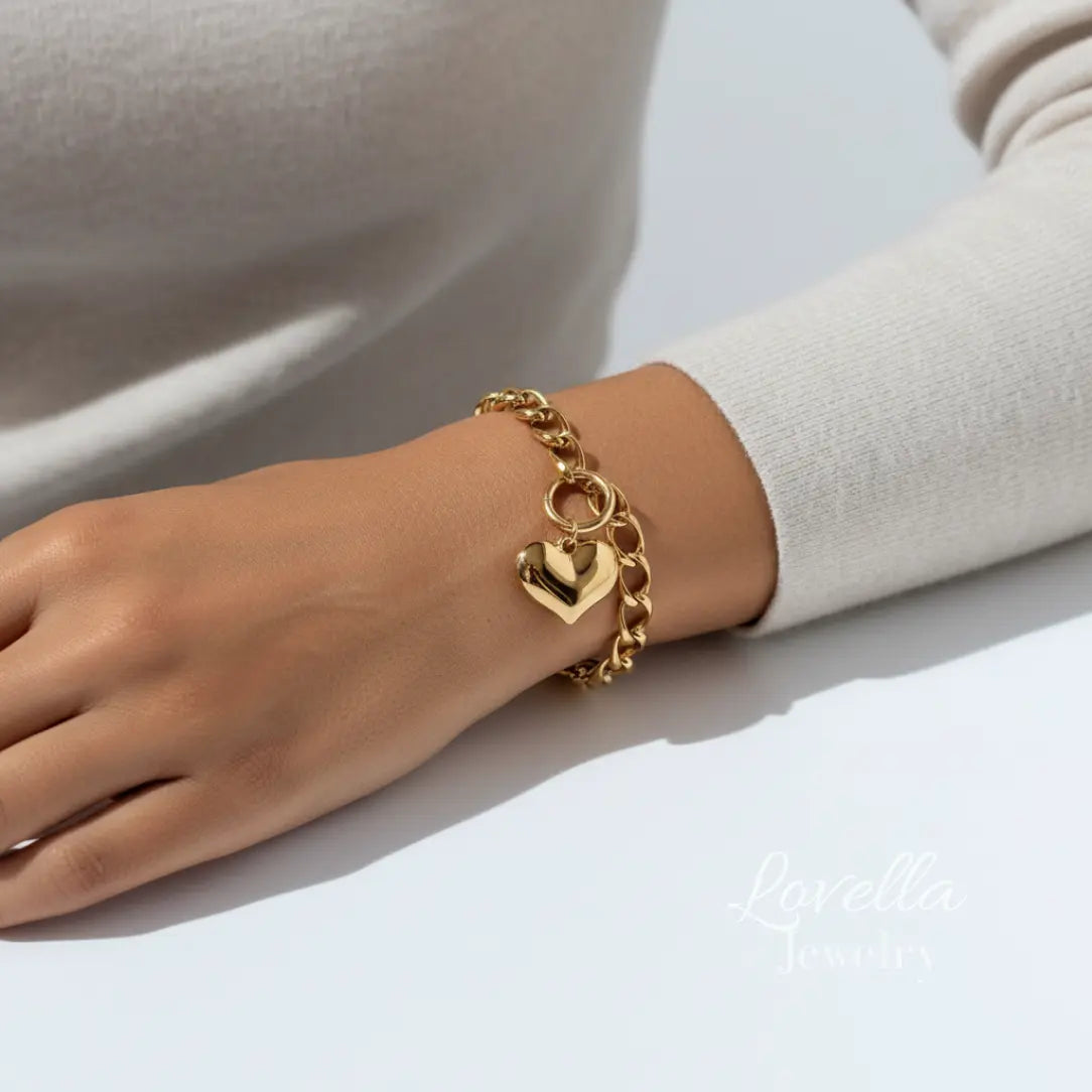 Gold chain bracelet with a heart charm on a wrist against a neutral background