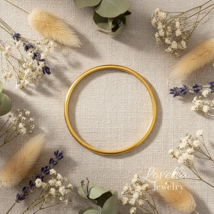 Gold bangle on a textured surface with dried flowers and leaves