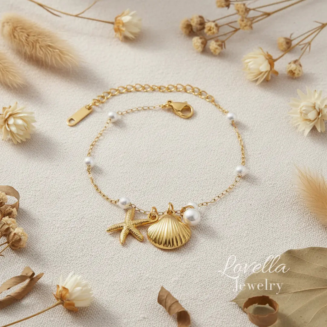 Gold bracelet with shell and starfish charms on a beige surface with dried flowers and leaves.