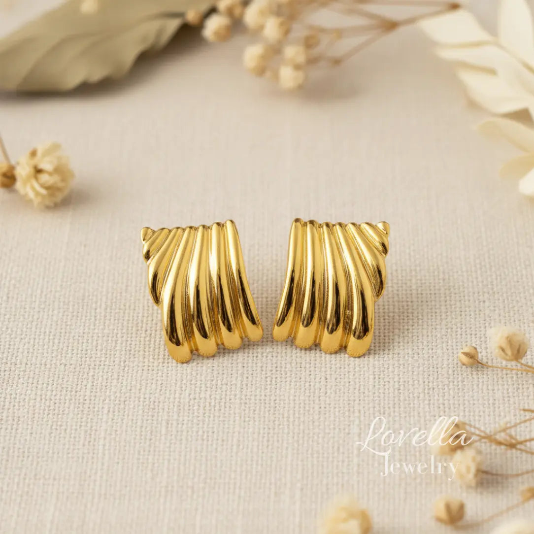 Gold earrings on a textured beige surface with dried flowers.