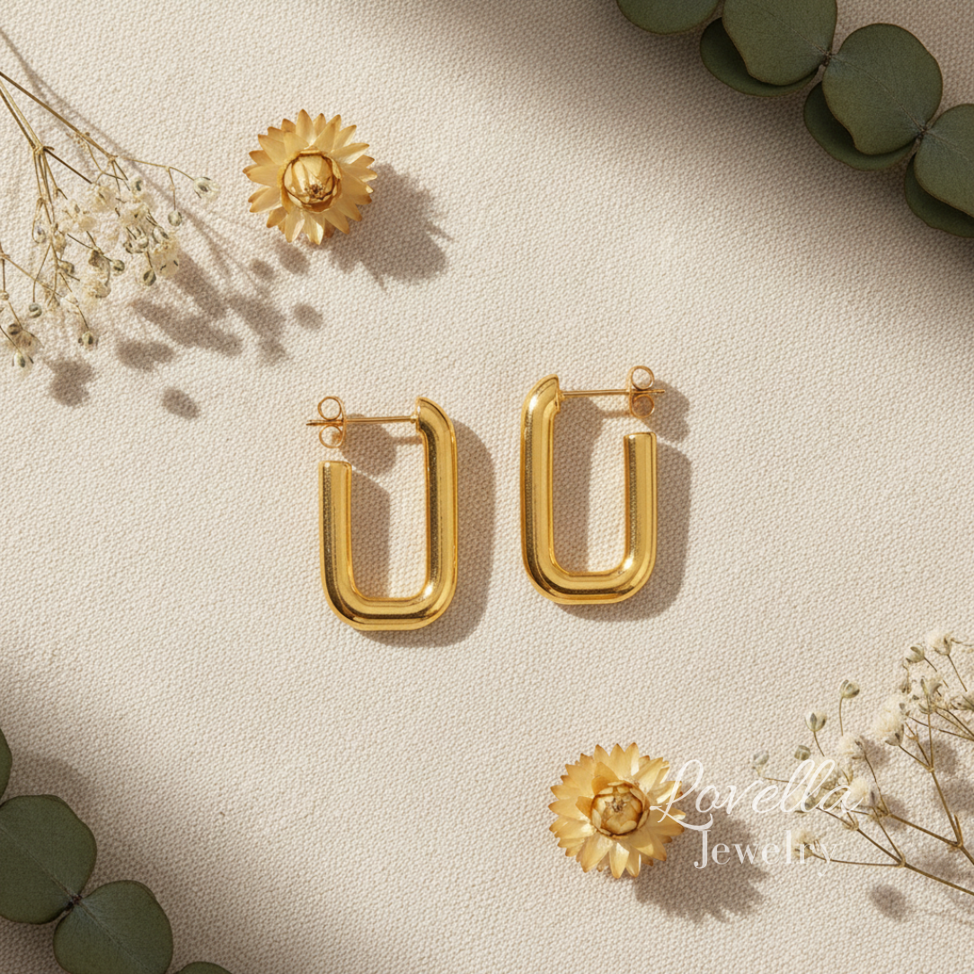 Gold hoop earrings on a light beige surface with green leaves and flowers.