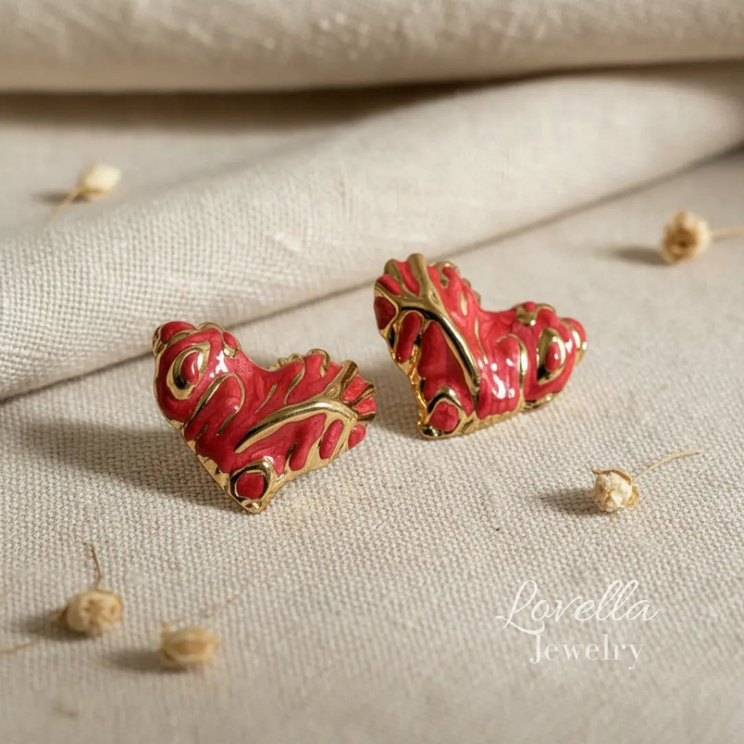 Red and gold earrings on a textured beige surface with 'Lovella Jewelry' branding.