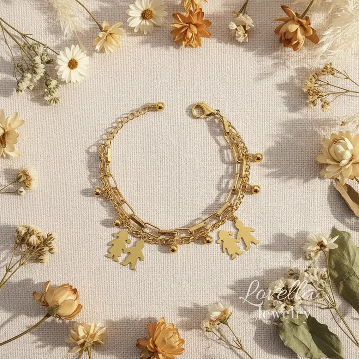 Gold bracelet with leaf charms on a background of dried flowers, featuring the brand 'Lovella Jewelry'.