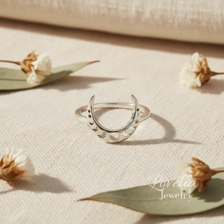 Silver crescent moon ring on a beige fabric background with dried flowers and leaves.