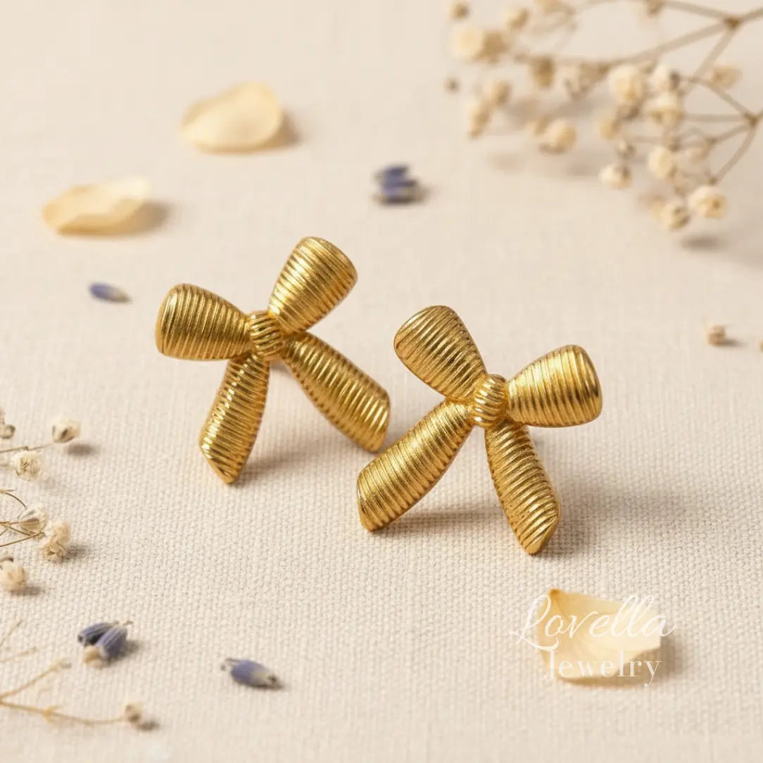 Gold bow-shaped earrings on a beige background with dried flowers.