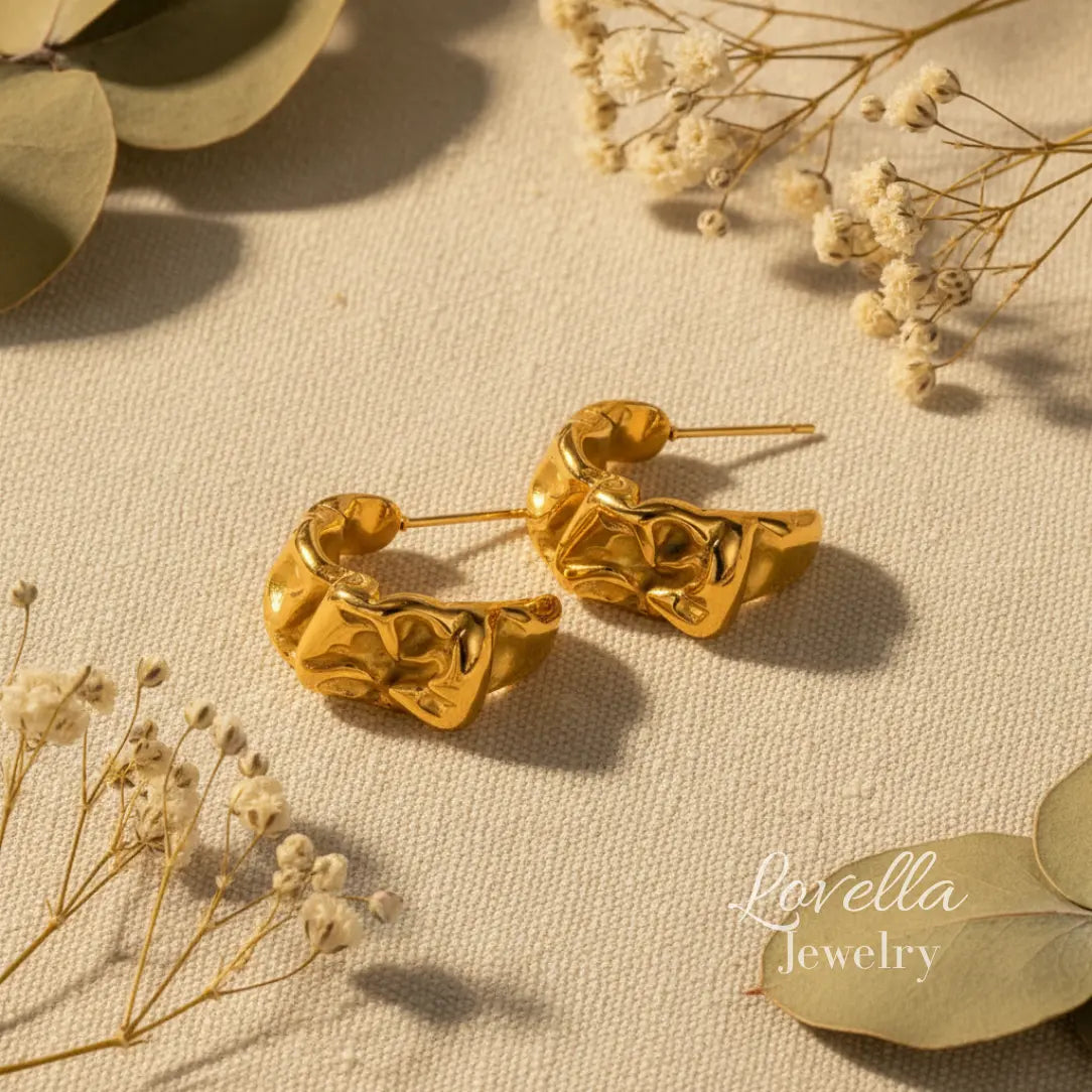 Gold hoop earrings on a textured surface with dried flowers and leaves.