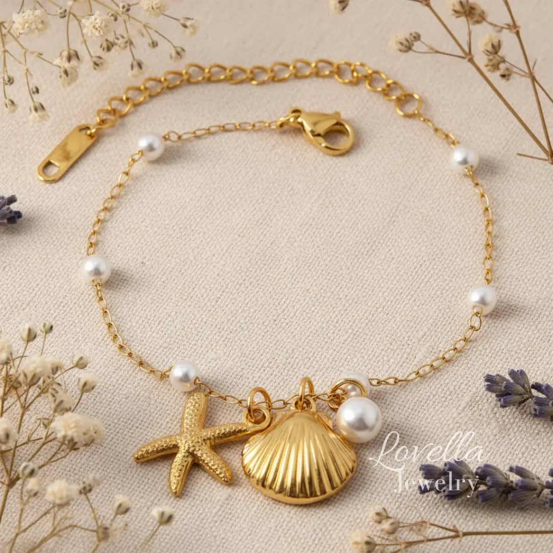 Gold bracelet with starfish, shell, and pearl charms on a beige background with dried flowers.