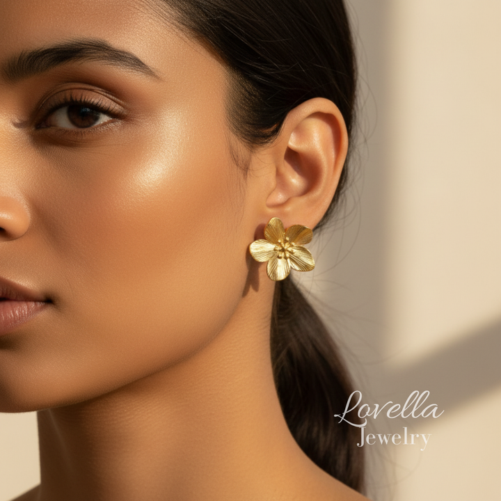 Close-up of a woman wearing gold flower earrings with 'Lovella Jewelry' branding.