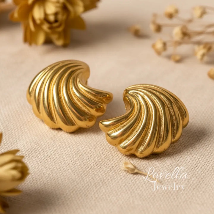 Gold earrings with a textured design on a beige fabric background, featuring Lovella Jewelry logo.