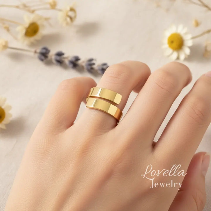 Gold ring on a finger with 'Lovella Jewelry' branding, against a soft floral background.