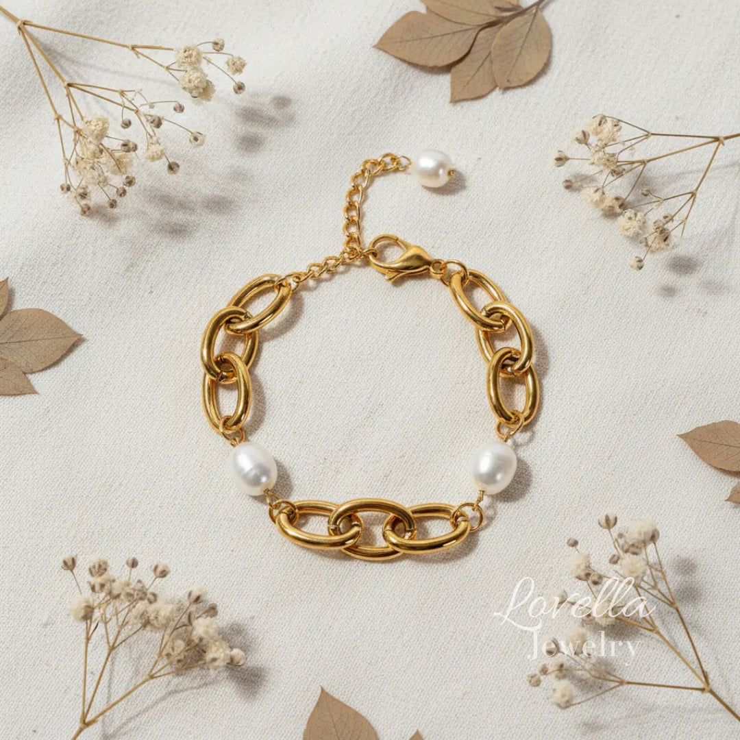 Gold chain bracelet with pearls on a light background with dried flowers and leaves.