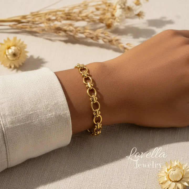 Gold bracelet on a wrist with decorative elements and 'Lovella Jewelry' branding.