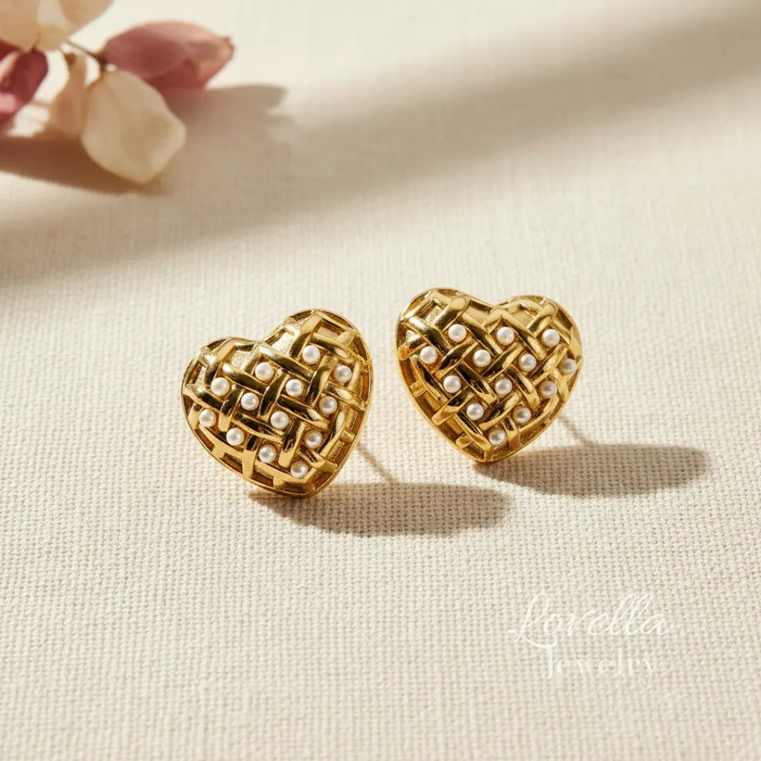 Heart-shaped gold earrings with pearl details on a beige fabric background