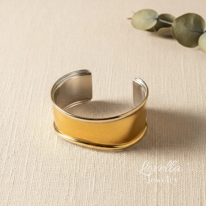 Gold and silver cuff bracelet on a beige fabric background with 'Lovella' branding.