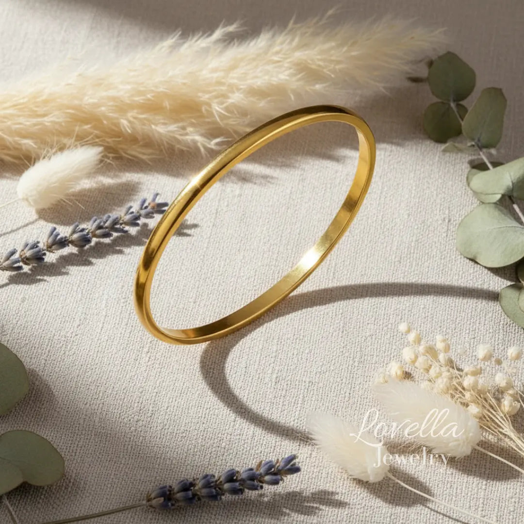 Gold bangle on a light fabric background with dried flowers and leaves