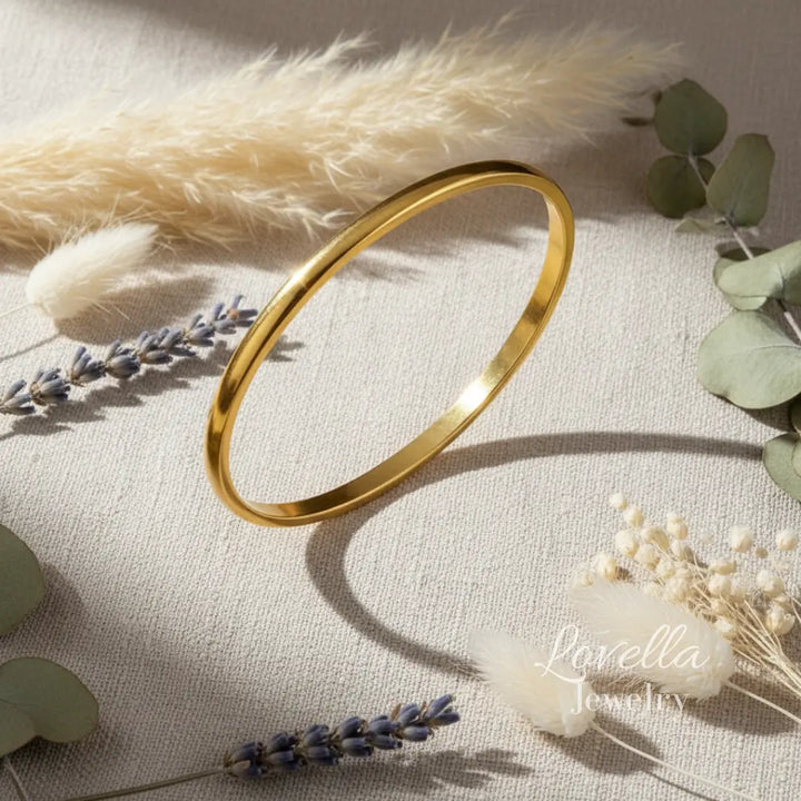 Gold bangle on a light fabric background with dried flowers and leaves