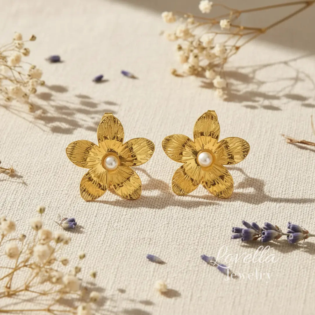 Gold flower-shaped earrings with pearl centers on a beige surface with dried flowers.