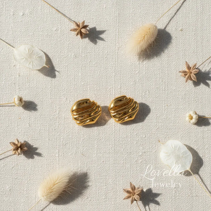 Gold chunky swirl stud earrings on cream linen background with dried flowers and Lovella Jewelry logo