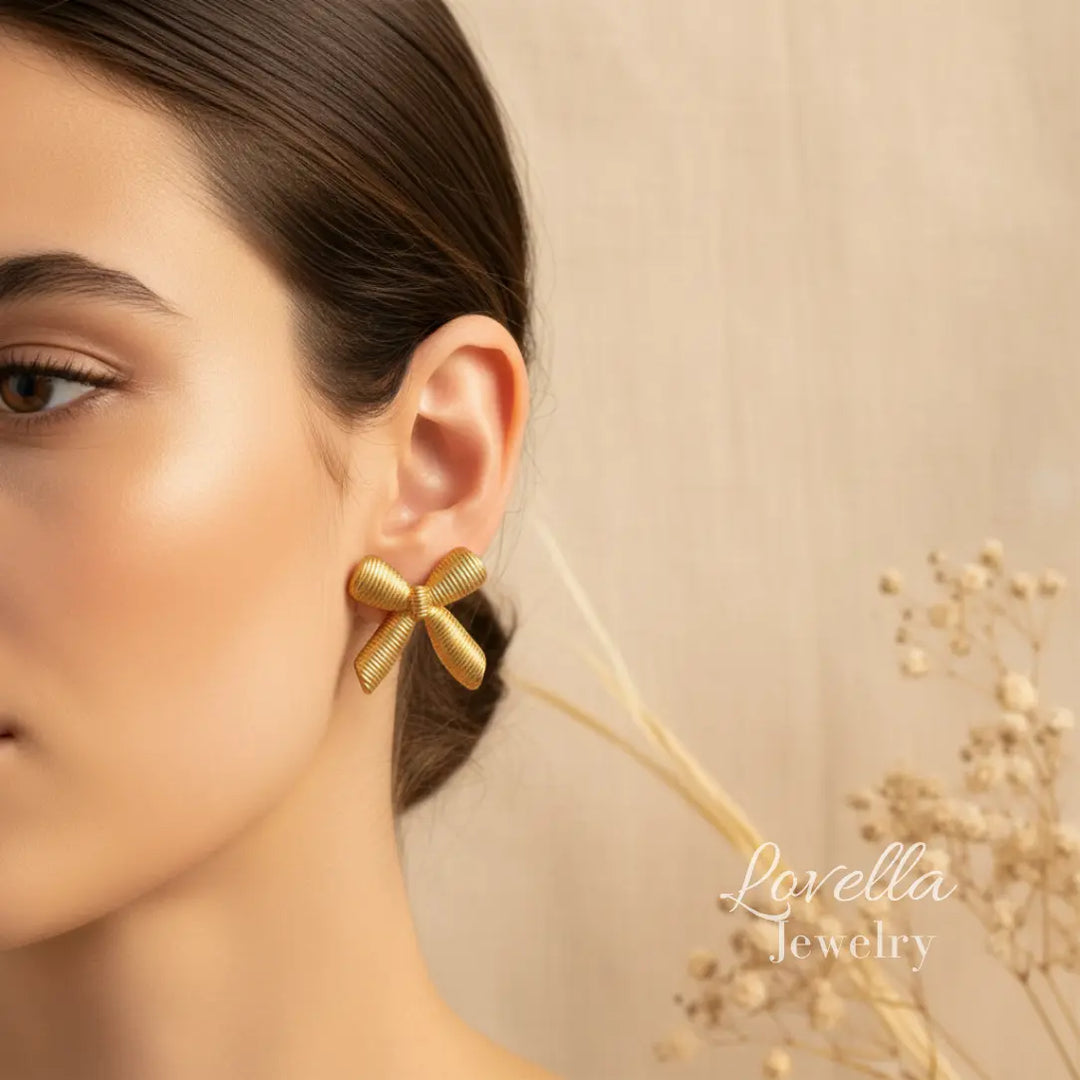Gold bow-shaped earrings worn by a model with a neutral background and 'Lavella Jewelry' branding.
