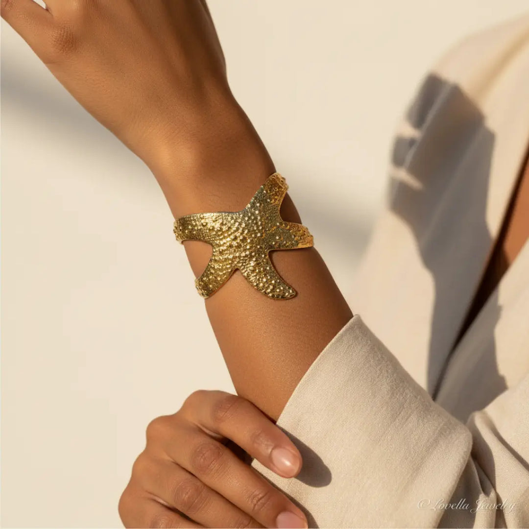Gold starfish bracelet on a wrist against a neutral background