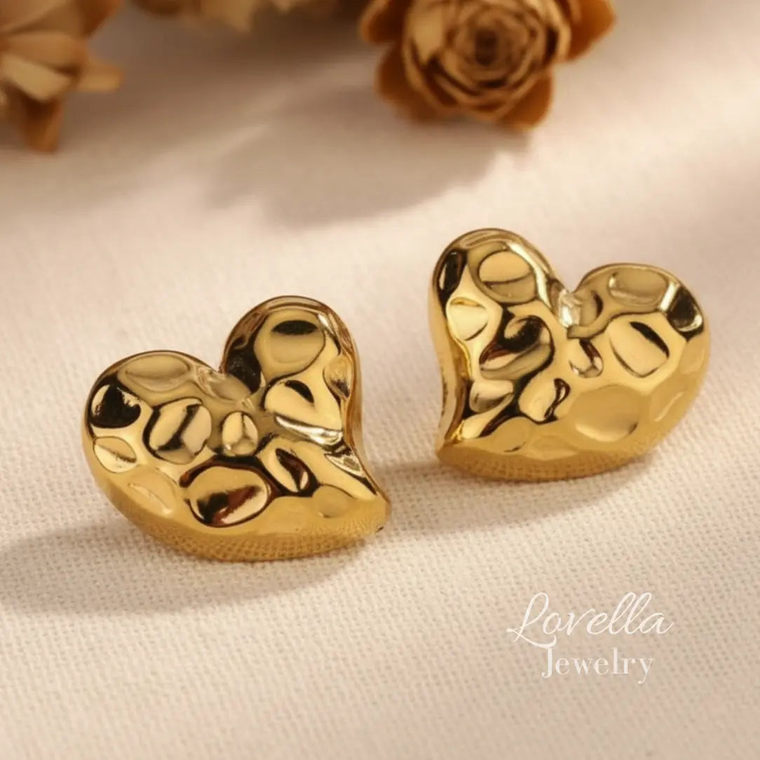 Gold heart-shaped earrings on a light fabric background with 'Lovella Jewelry' branding.