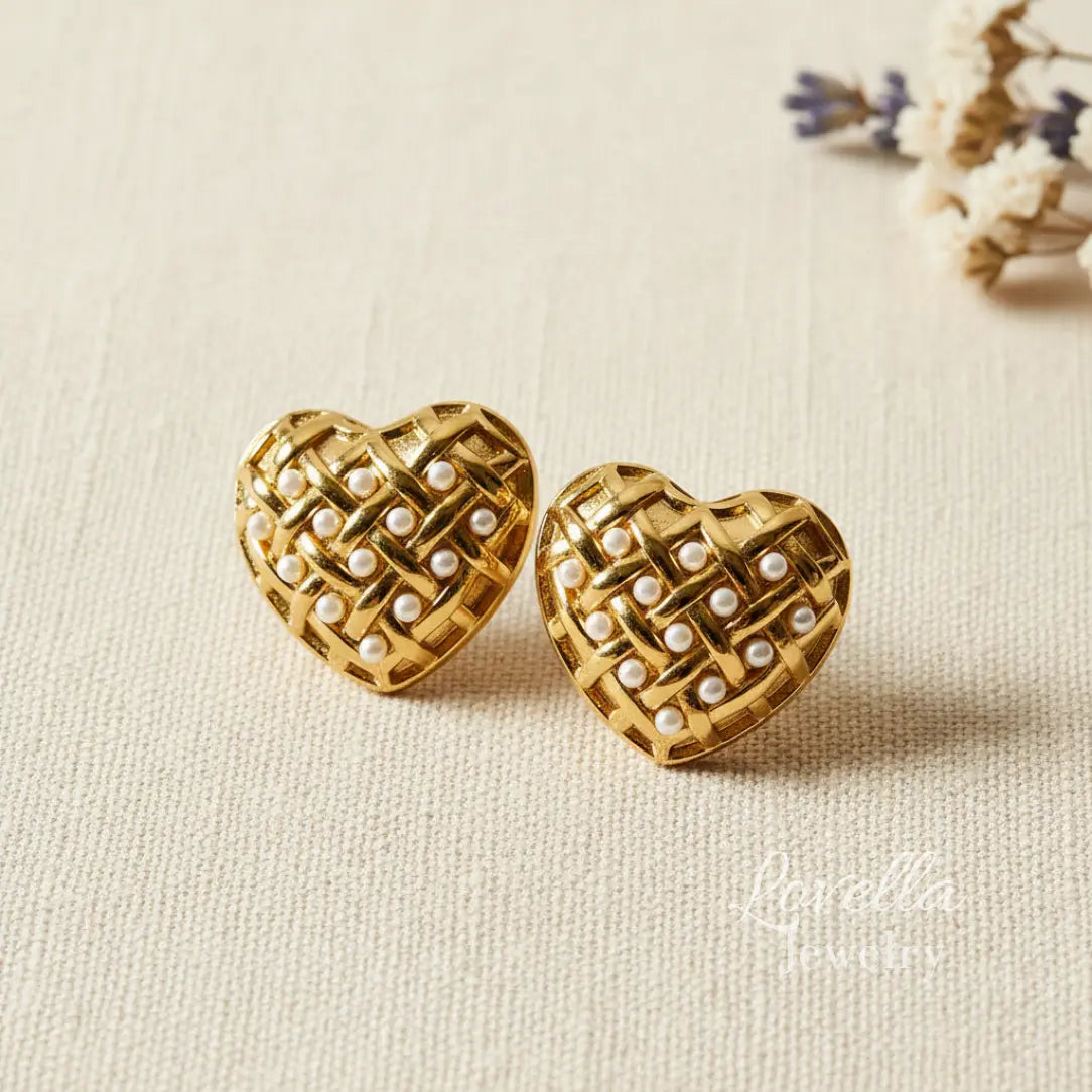 Gold heart-shaped earrings with pearl detailing on a beige fabric background