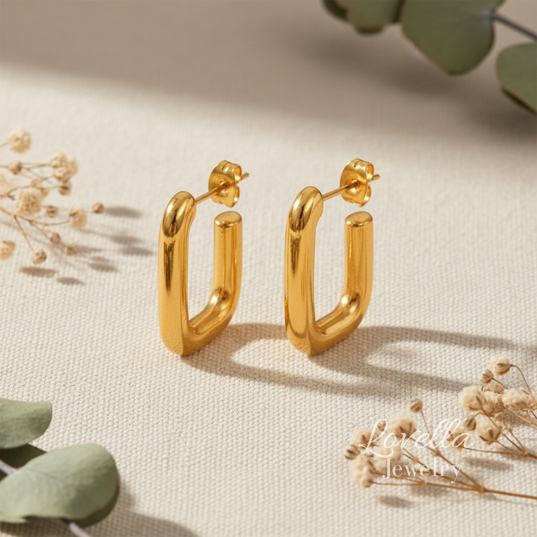 Gold hoop earrings on a light beige surface with dried flowers and green leaves.