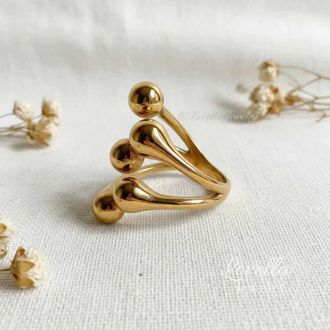 Gold-tone stainless steel bubble ring photographed flat lay on neutral fabric with dried flowers and minimal styling props.