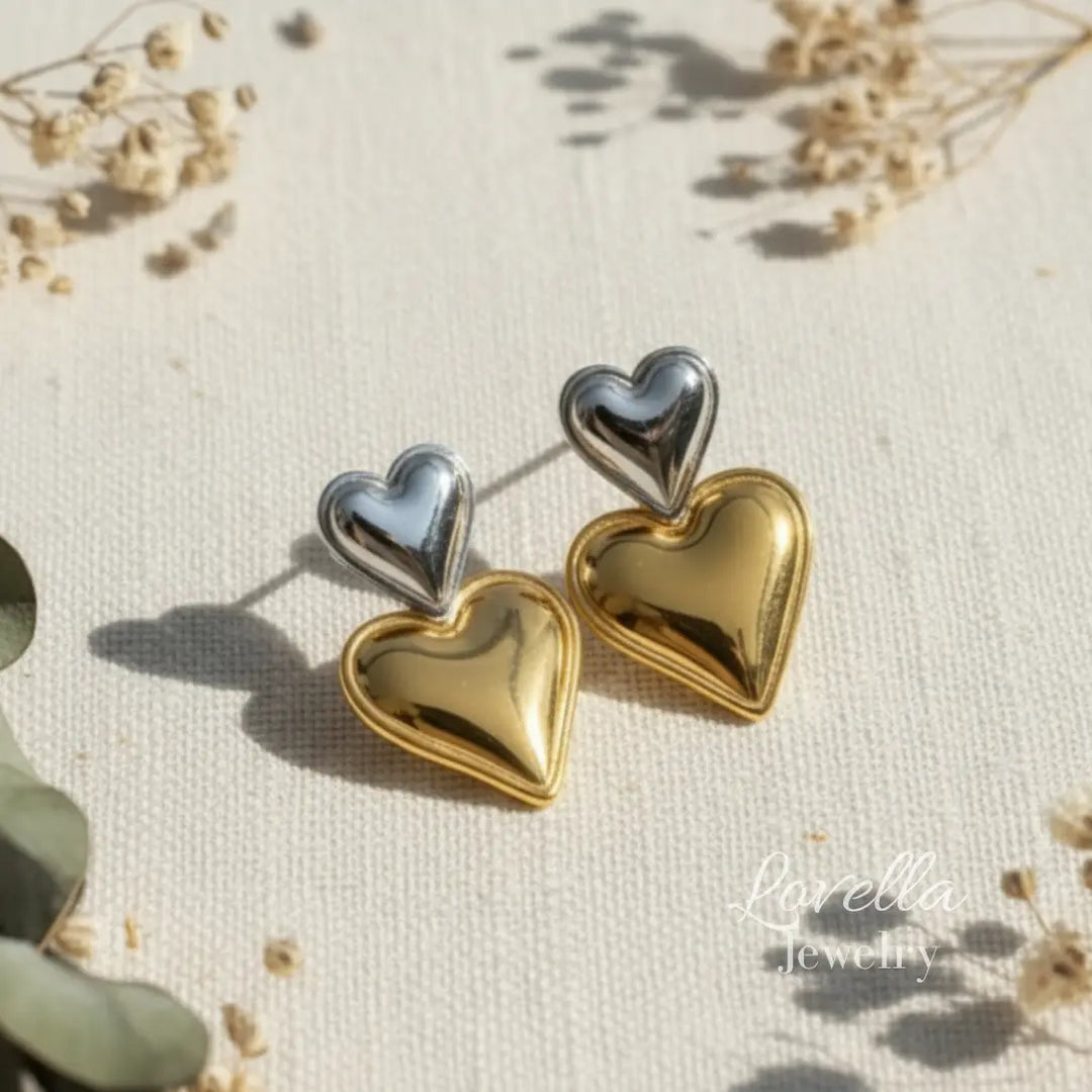 Heart-shaped earrings in gold and silver on a textured surface with 'Lovella Jewelry' branding.
